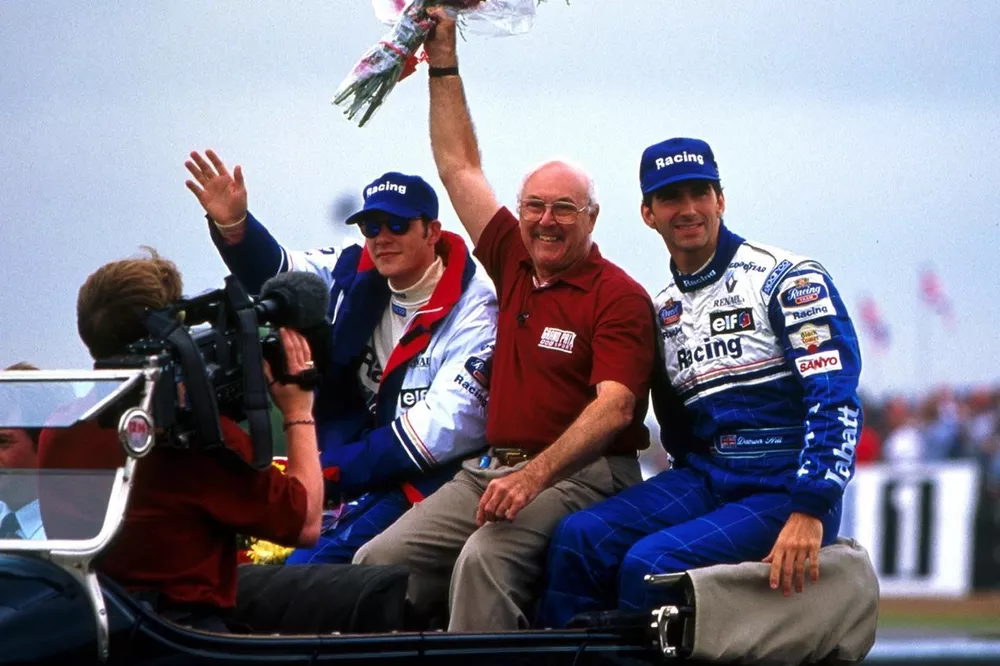 BBC Grand Prix commentator Murray Walker waves to the crowds. Beside him are Rothmans Williams drivers Damon Hill and Jacques Villeneuve 