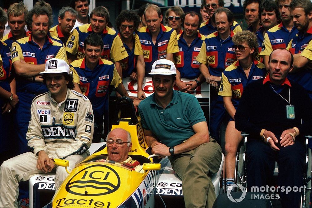 BBC TV commentator Murray Walker in the Williams FW11 sits with the regular drivers Nelson Piquet and Nigel Mansell. Team Owner Frank Williams sits to the right.
