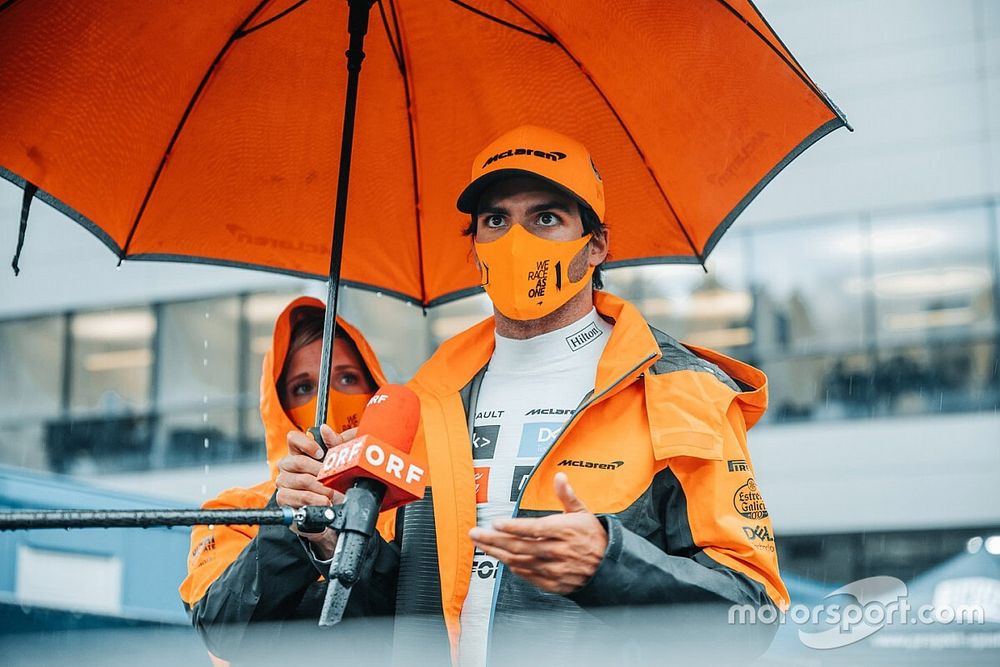 Carlos Sainz Jr., McLaren, shelters under an umbrella 