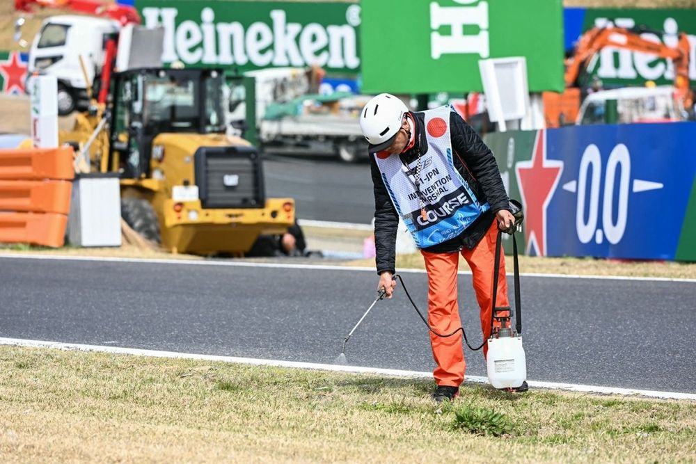 A track marshal waters down the dried out grass along the side of the track
