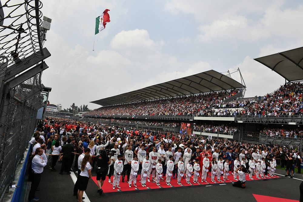 Los pilotos se paran con las mascotas de Grid Kid durante el himno nacional mientras un helicóptero ondea la bandera antes de la salida