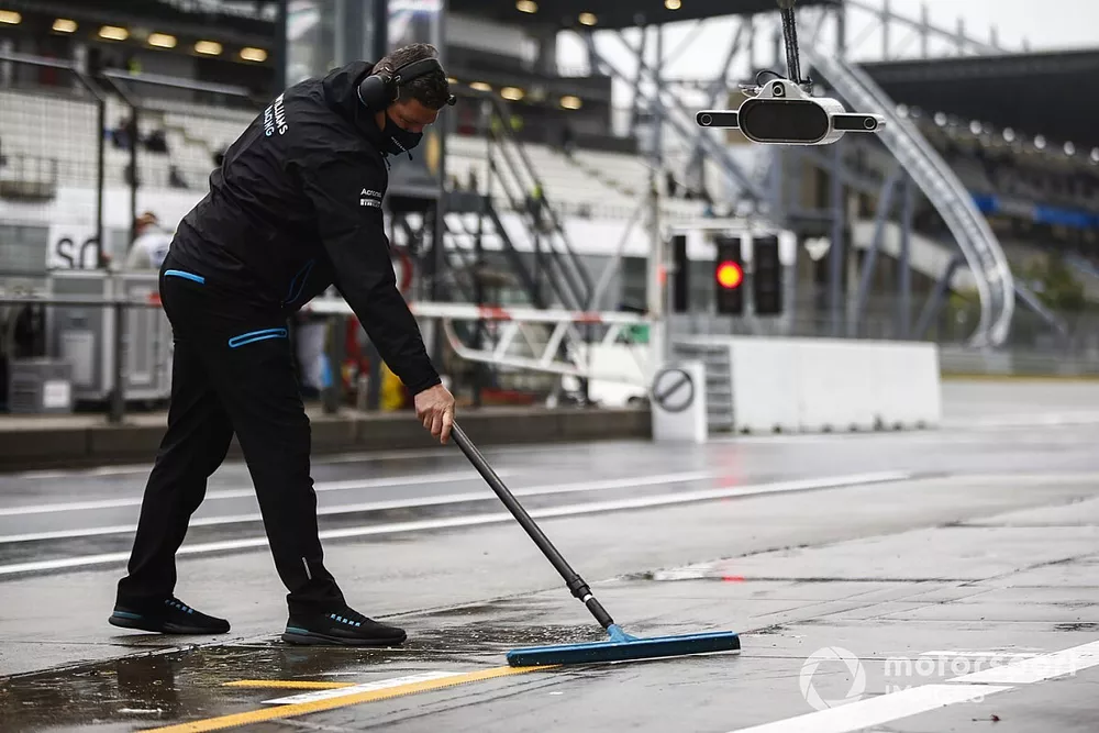 A member of the Williams Racing team shifts water in the pitlane
