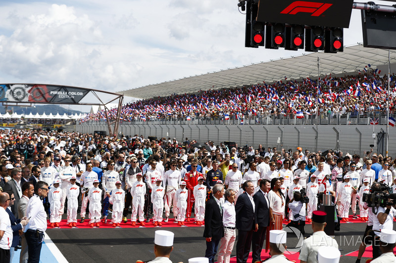 The drivers stand behind the Grid Kid mascots as the national anthem is sung prior to the start