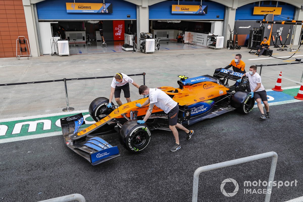 McLaren personnel wheel a car along the pitlane