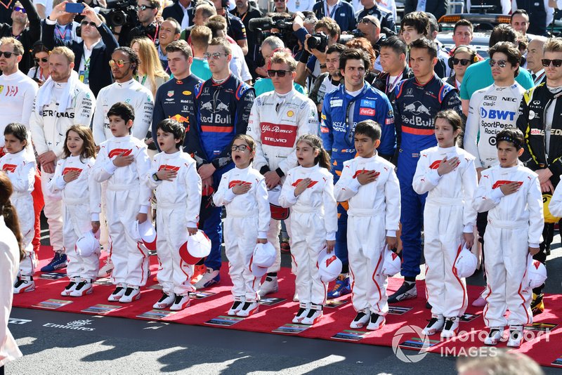The drivers and Grid Kids stand for the national anthem prior to the start