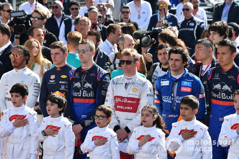 The drivers and Grid Kids stand for the national anthem prior to the start