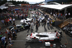 Brendon Hartley poses, a Porsche 919 sportcar. A Bentley, BMW V12 LMR, Group C Porsche, BMW CSL, Ferrari 512 and Porsche 917 line-up behind