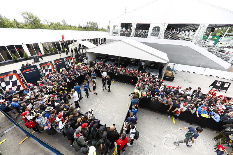 Fernando Alonso, McLaren, Carlos Sainz Jr., Renault Sport F1 Team, and Stoffel Vandoorne, McLaren, sign autographs for fans. Photographers, including Andy Hone, are among the melee in the enclosure