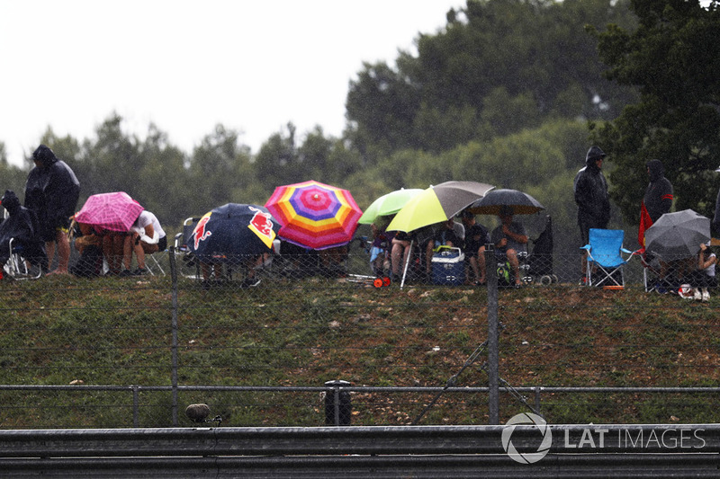 Los espectadores se resguardan de la lluvia bajo los paraguas
