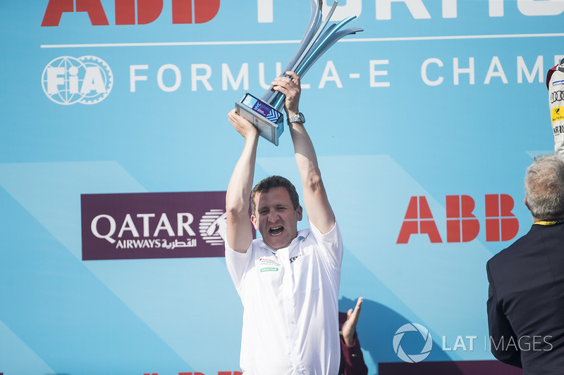 An Audi team member celebrates with the winning team trophy on the podium