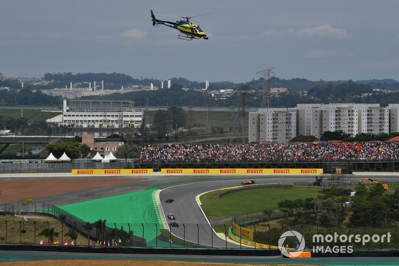 An HelibrÃ¡s AS-350B3 Esquilo (license built Eurocopter AS-350 Squirrel) camera helicopter in the same colours as the helmet of Ayrton Senna flies over as the cars head around the formation lap