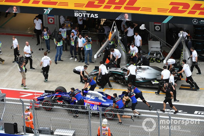 The car of Daniil Kvyat, Toro Rosso STR14, is pushed past Lewis Hamilton, Mercedes AMG F1 W10, in the pits