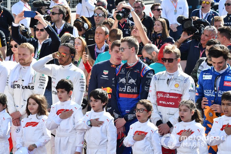 The drivers and Grid Kids stand for the national anthem prior to the start