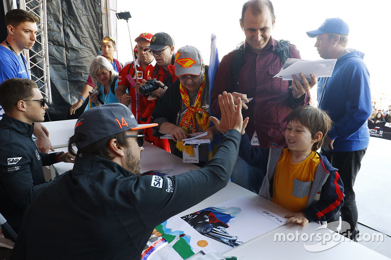 Fernando Alonso, McLaren, gives a high-five to a young fan, as Stoffel Vandoorne, McLaren, signs autographs