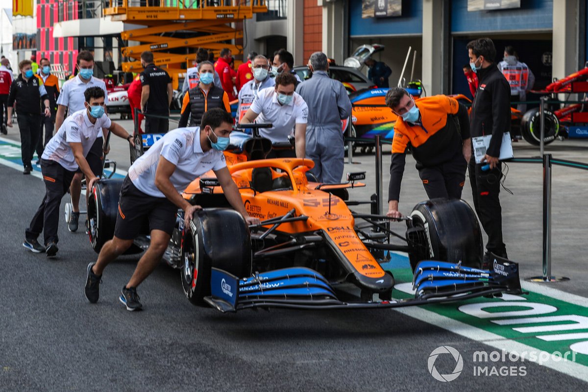McLaren personnel wheel a car along the pitlane