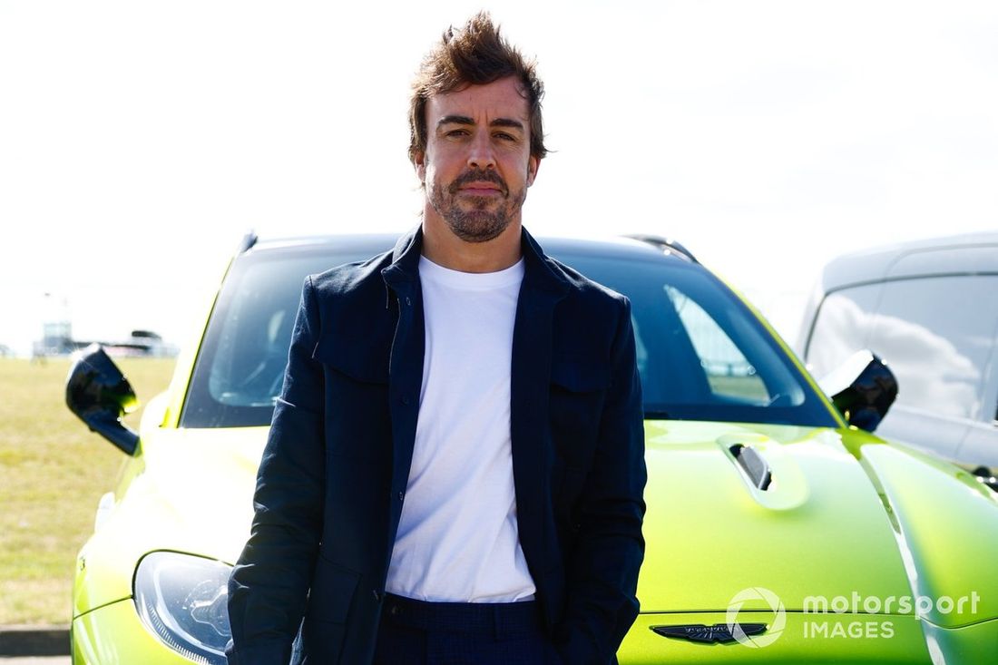 Fernando Alonso, Aston Martin F1 Team, trzyma kask, opierając się o przód Astona Martina DBX.
