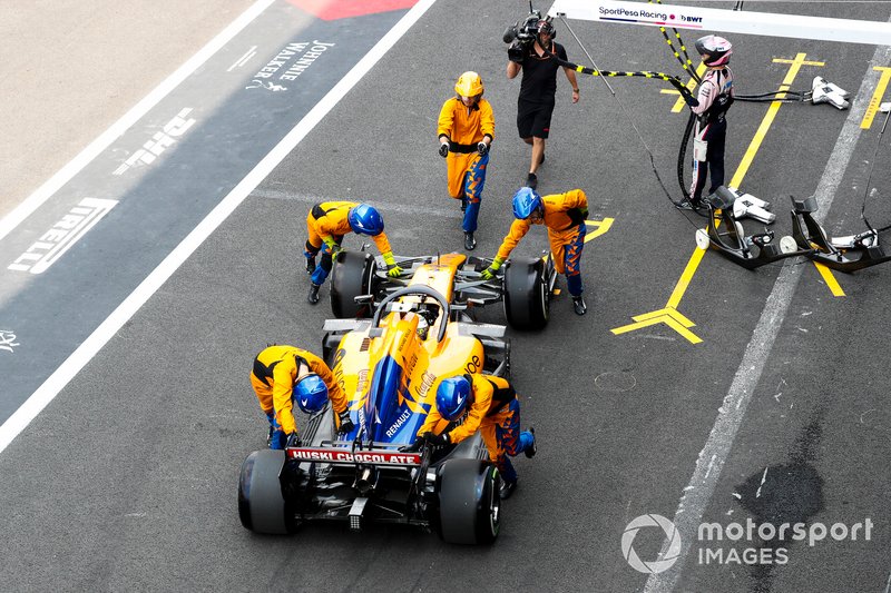 Mechanics push back Lando Norris, McLaren in the pit lane