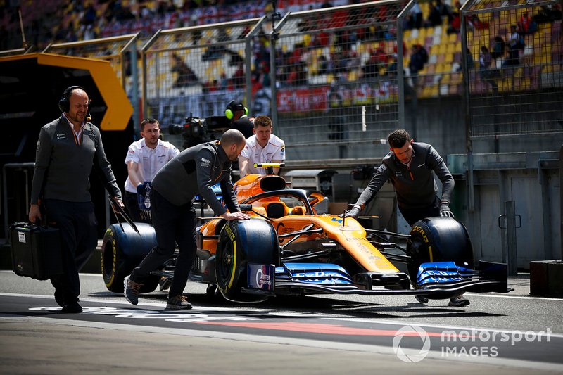 McLaren mechanics move the car of Lando Norris, McLaren MCL34, through the pit lane