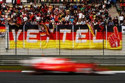 A Ferrari flashes by a stand containing a large number of Sebastian Vettel, Ferrari, fans