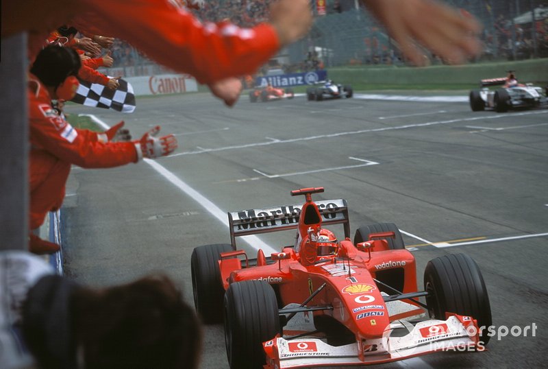 Michael Schumacher, Ferrari F2002, takes the chequered flag and celebrates with the Ferrari team