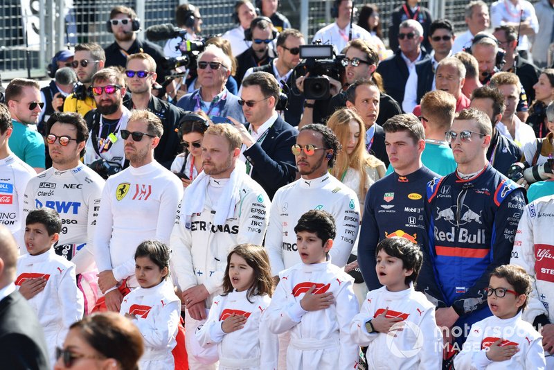The drivers and Grid Kids stand for the national anthem prior to the start