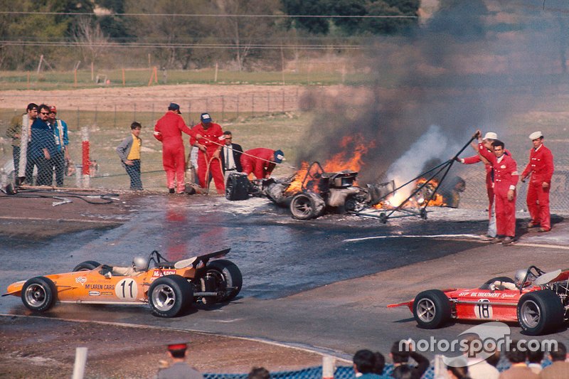 Bruce McLaren, McLaren M14A Ford and Mario Andretti, March 701 Ford drive past the flame engulfed cars of Jacky Ickx and Jackie Oliver