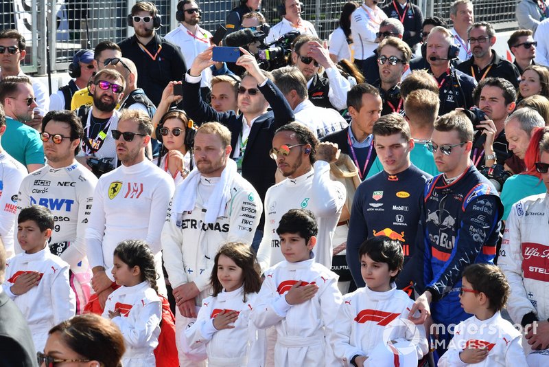 The drivers and Grid Kids stand for the national anthem prior to the start
