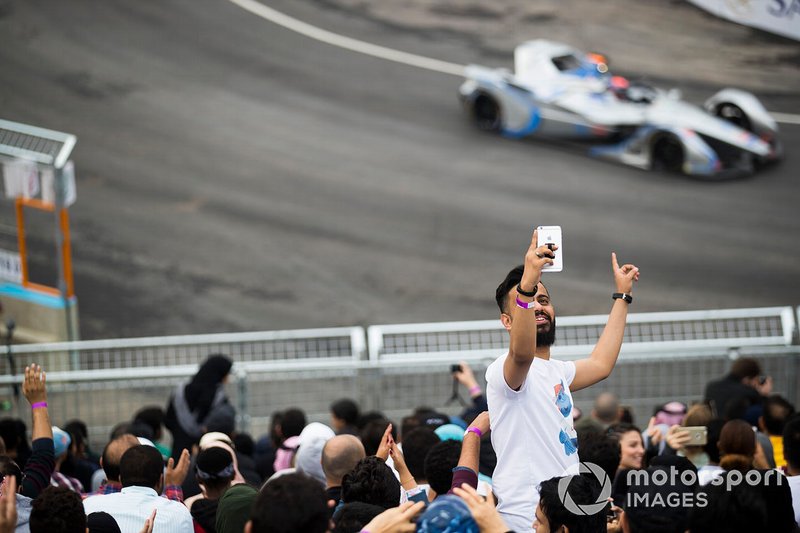 un fan scatta un selfie con una monoposto che transita alle sue spalle