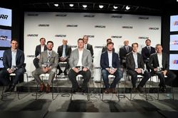 Ejecutivos y pilotos NASCAR se sientan en el escenario durante una conferencia de prensa que los cam