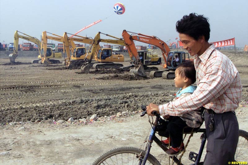 A Chinese father and child pass heavy machines rolling during the Shanghai Circuit ground-breaking ceremony October 17, 2002.