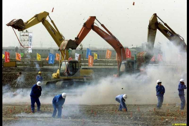 Chinese workers light firecrackers as heavy machines rev their engines during the Shanghai Circuit ground-breaking ceremony October 17, 2002.