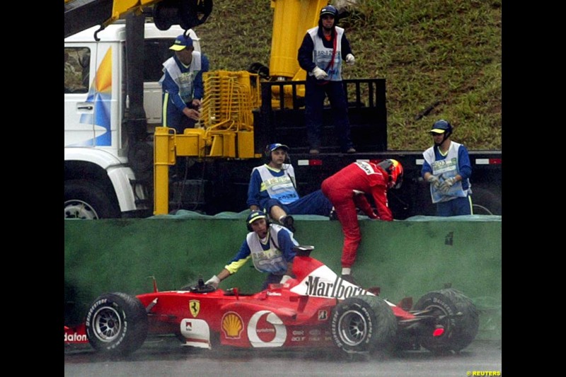 Michael Schumacher, Ferrari, climbs over the barriers after crashing out of the Brazilian Grand Prix. Interlagos, Sao Paulo, April 6th 2003.