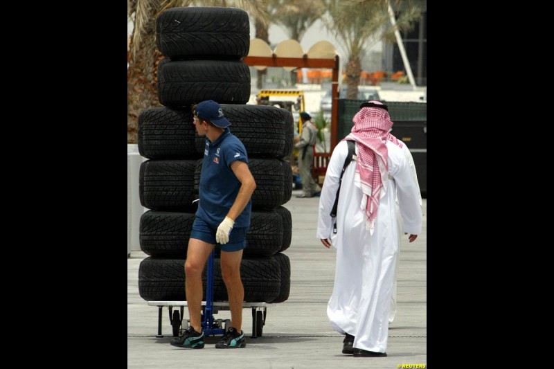 Sauber mechanic pulls a rack of tires as locals take a walk in the pitlane of the Bahrain International Circuit near the Bahrain capital of Manama, ahead of the first Bahrain Grand Prix. March 31st, 2004.