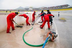 Oficiales de pista limpian el agua acumulada por la lluvia