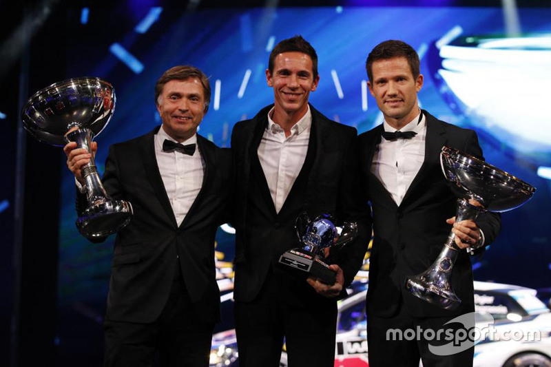 Sebastien Ogier and his co-driver Julien Ingrassia claim the WRC champion's trophy for the third year in succession, joined by VW boss Jost Capito.